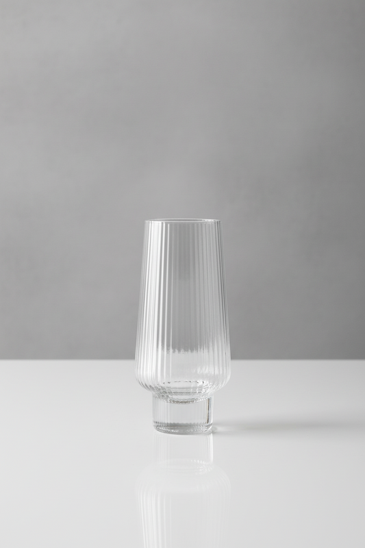 Clear glass held by a hand with red nail polish against a background of white plates and coasters.